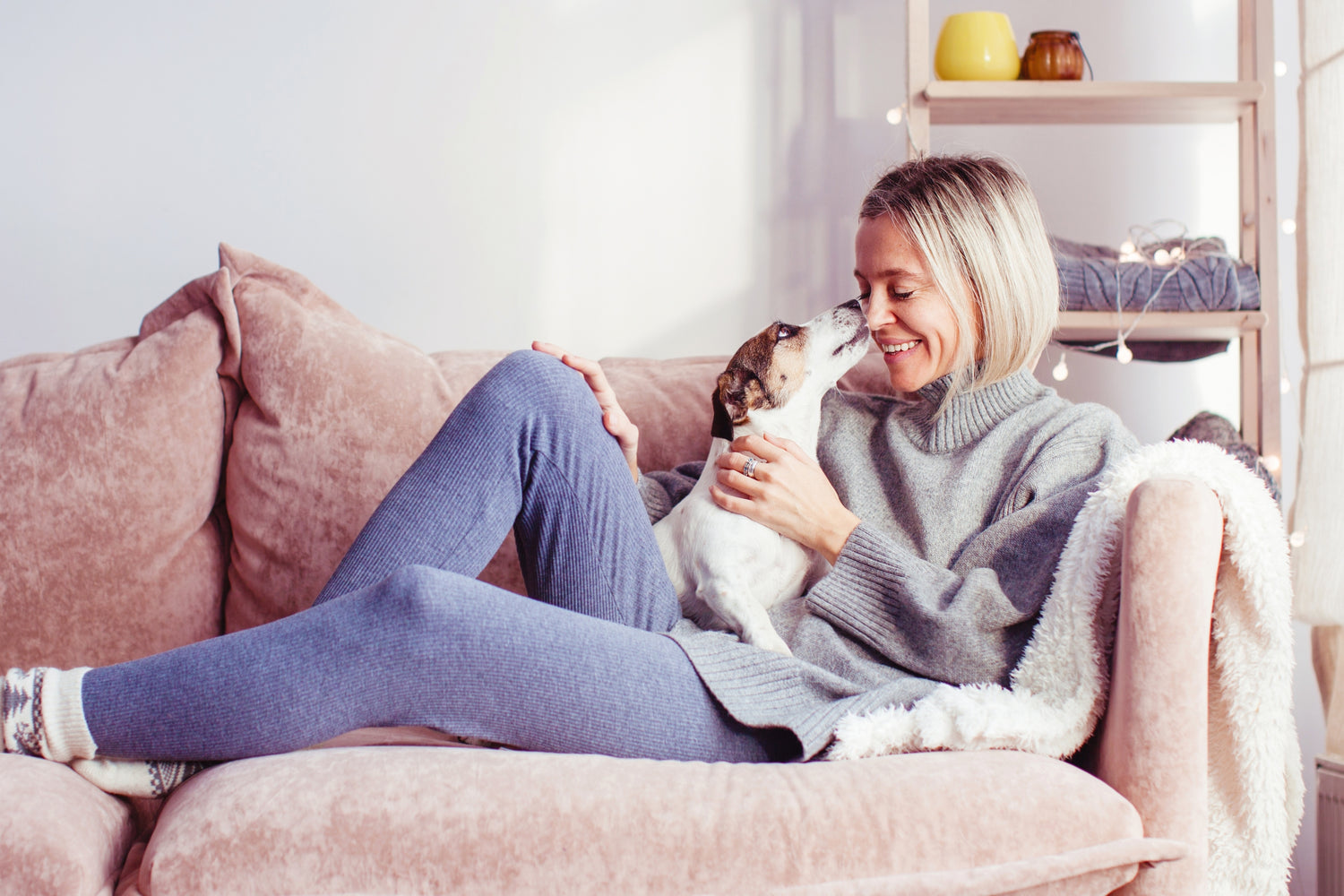 A smiling woman sitting on a comfortable couch with her loyal dog by her side. They both look relaxed and content.