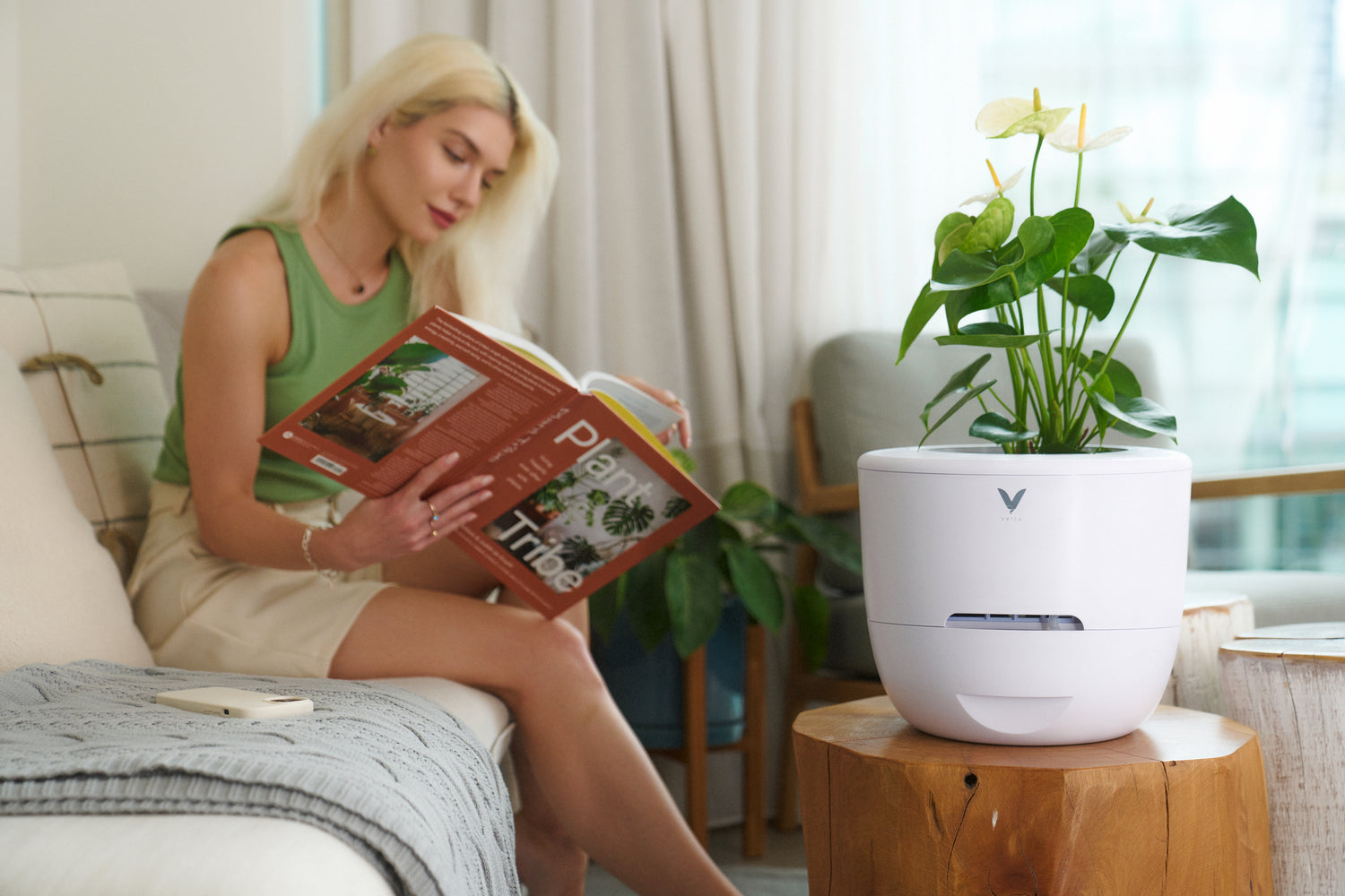 Woman reading on sofa, enjoying clean air beside Verta's Natural 4-in-1 Eco-Friendly Air Purifier utilizing plants as filters.